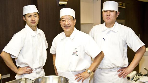 Drei Köche in Kochuniformen stehen in einer Küche.