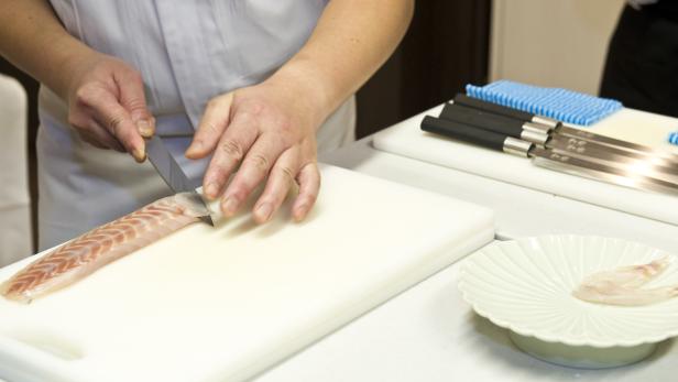 Ein Koch filetiert einen Fisch auf einem Schneidebrett.