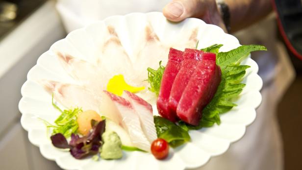 Ein Teller mit verschiedenen Sashimi-Sorten, garniert mit Wasabi und Gemüse.