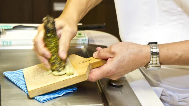 Ein Koch reibt frischen Wasabi auf einer Holzreibe.