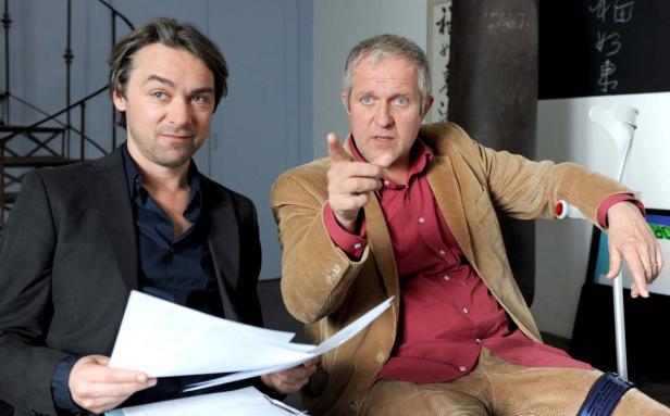 Zwei Männer sitzen zusammen, einer zeigt mit dem Finger auf etwas.