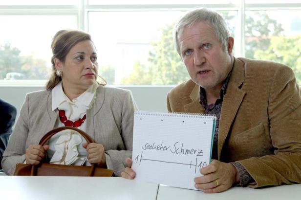 Ein Mann hält ein Schild mit der Aufschrift „Seelischer Schmerz“ neben einer Frau.