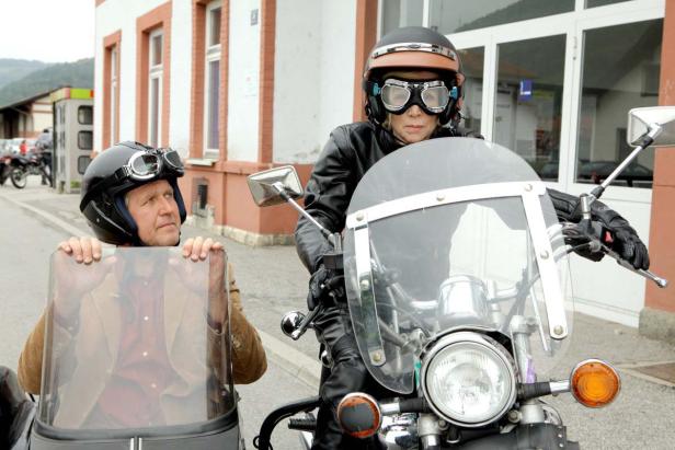 Eine Frau fährt ein Motorrad mit Beiwagen, in dem ein Mann sitzt.