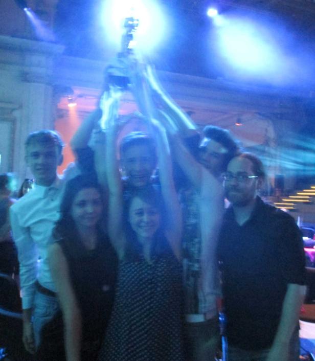 Eine Gruppe junger Leute feiert mit einer Trophäe in der Hand.