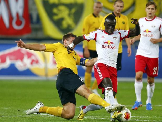 Ein Fußballspieler in Gelb grätscht nach einem Spieler in einem weißen und roten Trikot.