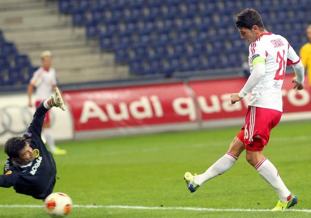 Ein Fußballspieler schießt den Ball, während der Torwart versucht, ihn abzuwehren.
