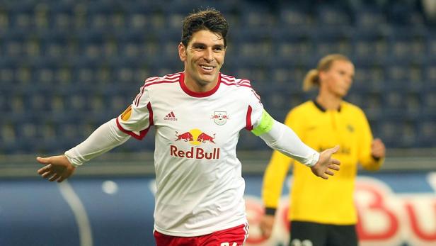 Ein lächelnder Fußballspieler im Trikot von Red Bull jubelt auf dem Spielfeld.