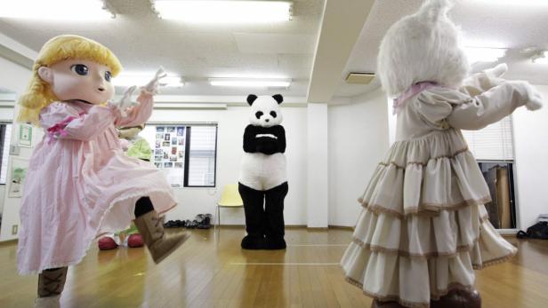 Drei Personen in Kostümen, darunter ein Panda, ein Mädchen und ein Hase, stehen in einem Raum.