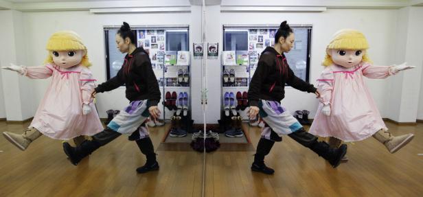 Eine Frau und eine Person im Puppenkostüm stehen vor einem Spiegel.