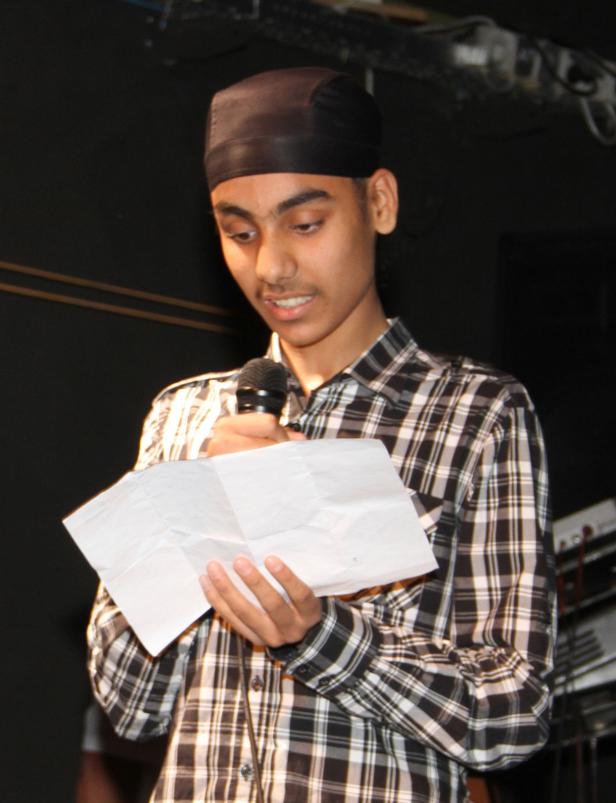 Ein junger Mann mit Kappe liest von einem Blatt Papier in ein Mikrofon.