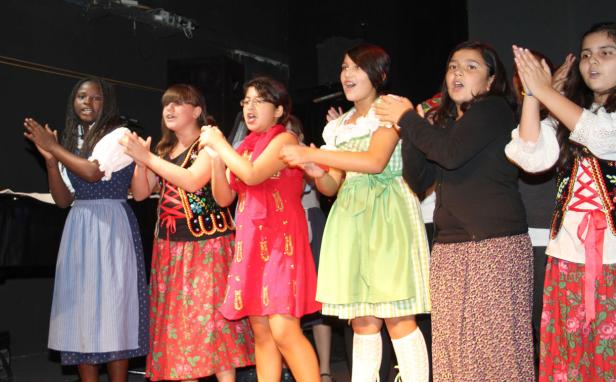 Eine Gruppe junger Frauen in Trachtenkleidung klatscht auf einer Bühne.