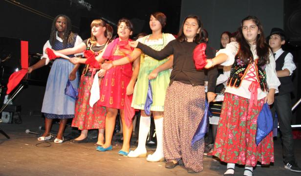 Eine Gruppe von Kindern in Trachten steht auf einer Bühne und hält Tücher in den Händen.