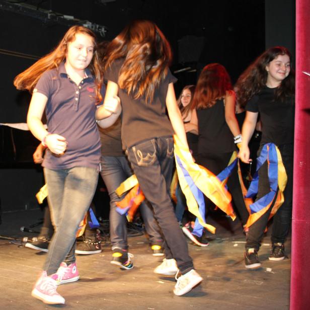 Eine Gruppe junger Mädchen tanzt mit bunten Bändern auf einer Bühne.