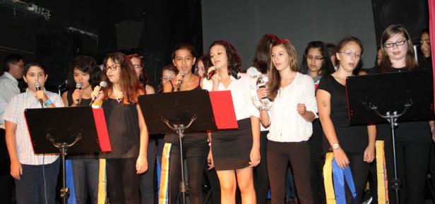 Eine Gruppe junger Leute singt gemeinsam auf einer Bühne.