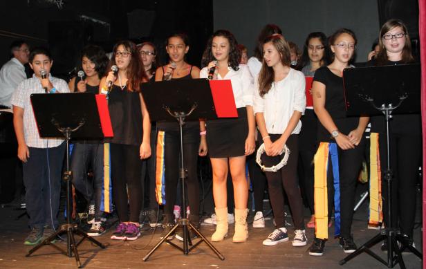 Eine Gruppe Jugendlicher steht auf einer Bühne und singt in Mikrofone.