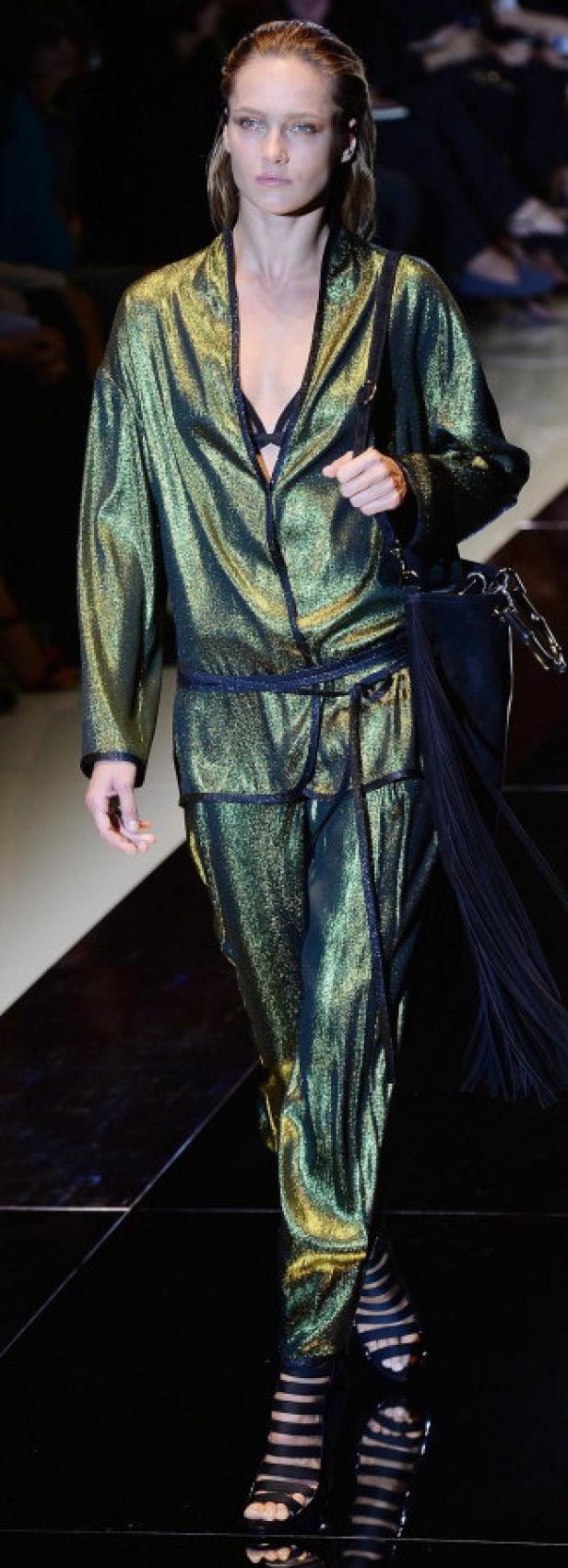 Eine Frau in einem glänzenden, grünen Hosenanzug auf einem Laufsteg.