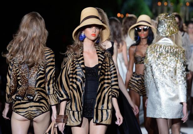 Models präsentieren Outfits mit Tiermustern und Hüten auf einem Laufsteg.