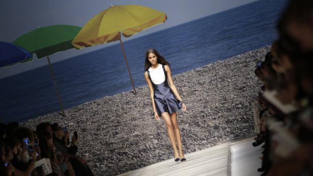 Eine Frau präsentiert ein Kleid auf einer Modenschau mit Strandkulisse.