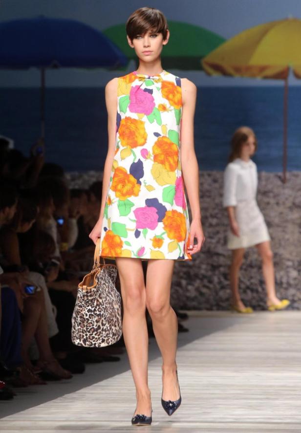 Eine Frau mit einem geblümten Kleid und einer Handtasche auf einem Laufsteg.