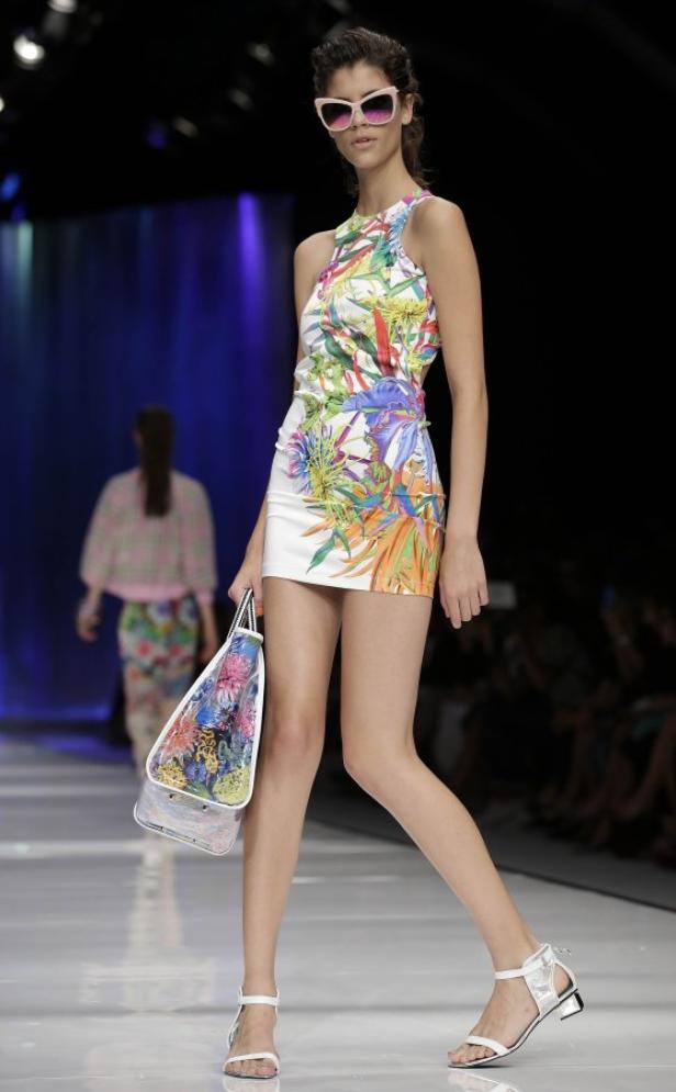 Eine Frau mit Sonnenbrille präsentiert ein kurzes, buntes Kleid auf dem Laufsteg.