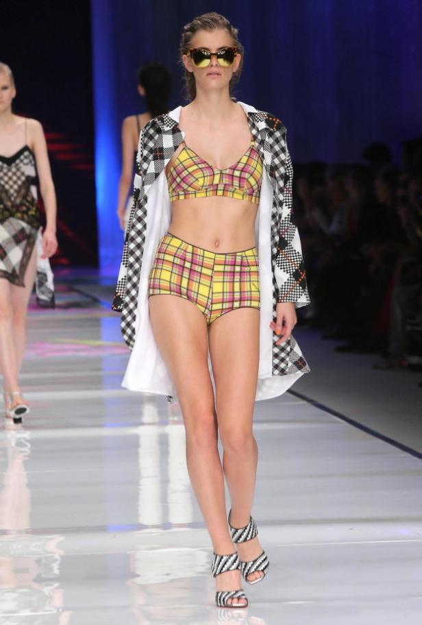 Eine Frau in gelb-kariertem Bikini und Mantel auf einem Laufsteg.