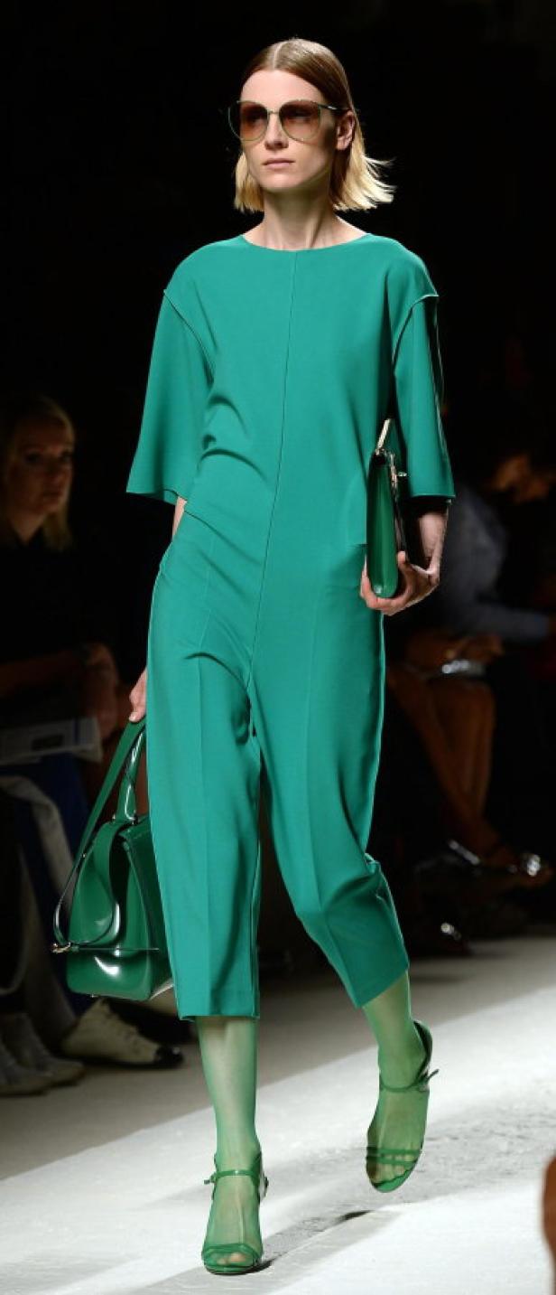 Eine Frau in einem grünen Hosenanzug mit passenden Accessoires auf dem Laufsteg.