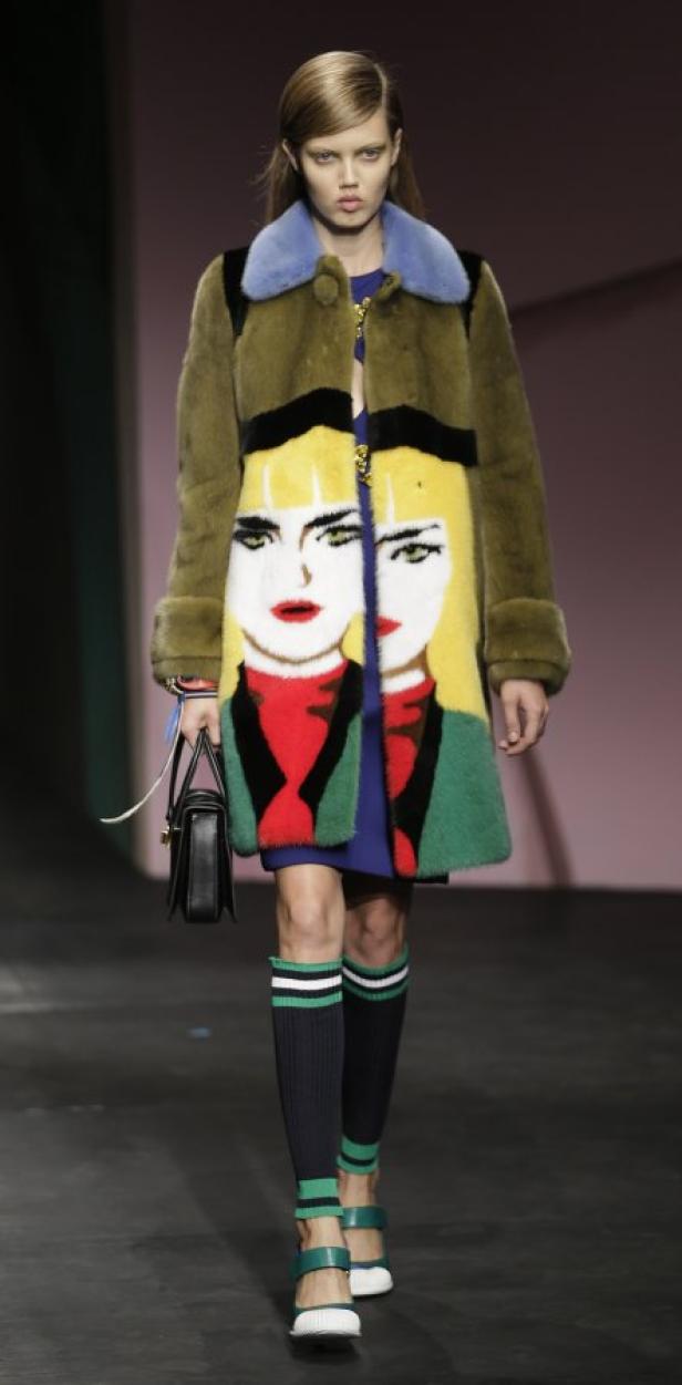 Ein Model präsentiert einen Mantel mit einem aufgedruckten Frauengesicht auf einem Laufsteg.