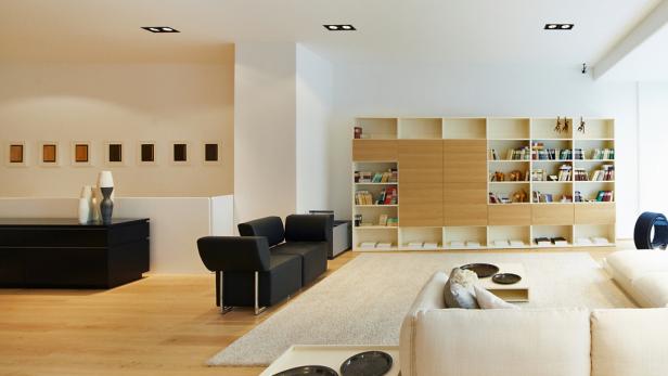 Ein modernes Wohnzimmer mit hellen Holzböden und einem großen Bücherregal.