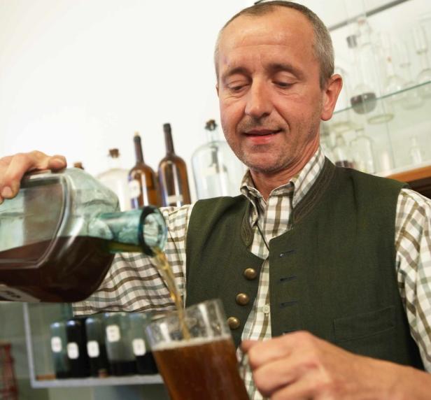 Ein Mann im Trachtenlook gießt ein Getränk aus einer Glasflasche in ein Glas.