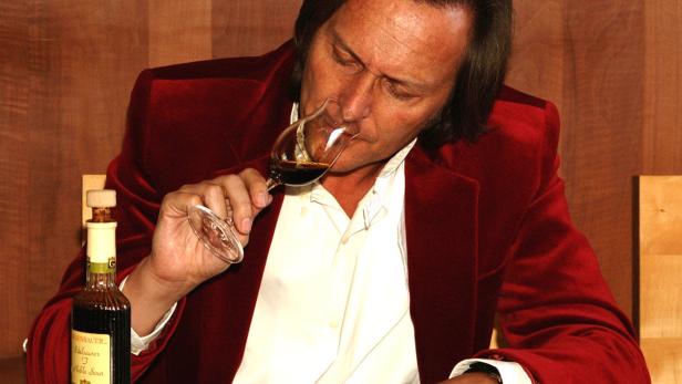 Ein Mann im roten Samtjackett riecht an einem Glas dunklen Balsamessig.