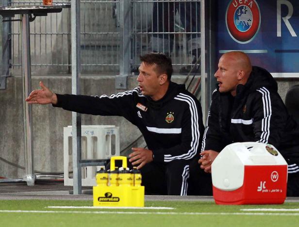 Zwei Trainer beobachten ein Fußballspiel von der Bank aus.