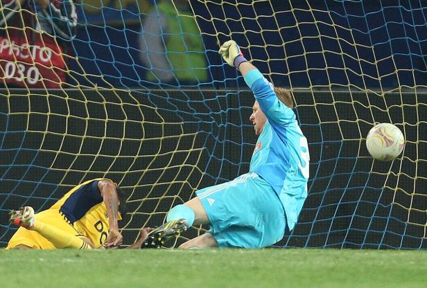 Ein Fußballtorwart wehrt einen Ball ab, während ein anderer Spieler am Boden liegt.