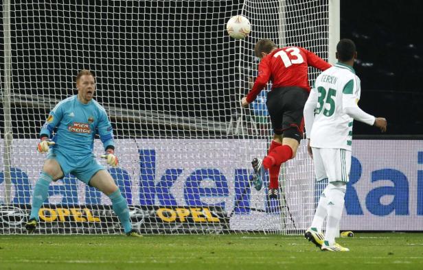 Ein Fußballspieler köpft den Ball vor dem Tor, während der Torwart zusieht.