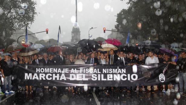 Eine Menschenmenge hält im Regen ein Banner mit der Aufschrift „Hommage an Fiscal Nisman, Marcha del Silencio“.