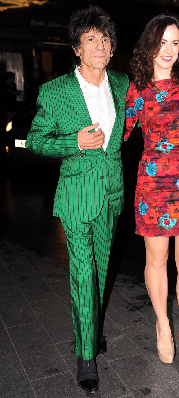 Ronnie Wood in einem grünen Anzug mit Nadelstreifen und eine Frau mit einem roten Blumenkleid.