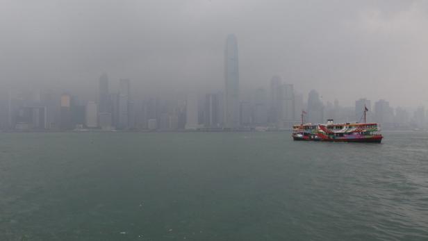 Eine bunte Fähre fährt vor der Skyline von Hongkong im Nebel.