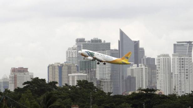 Ein Flugzeug von Cebu Pacific Air startet vor der Skyline einer Stadt.