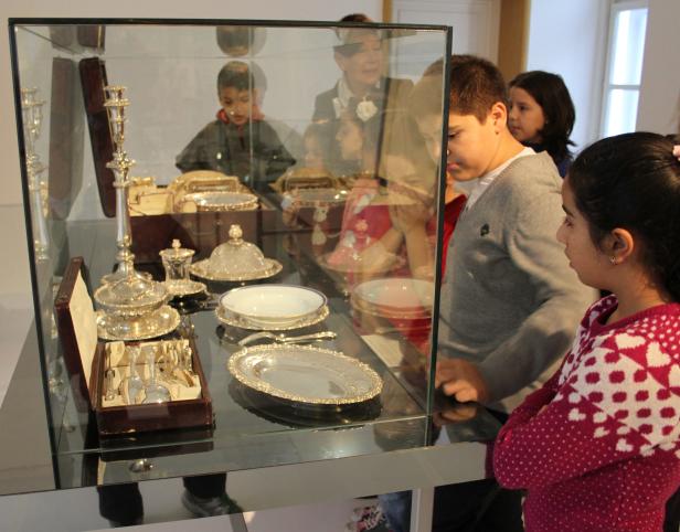 Kinder betrachten in einem Museum eine Vitrine mit silbernem Geschirr.