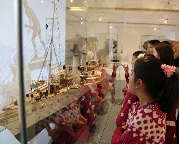 Eine Gruppe Kinder betrachtet das Modell eines Schiffes in einem Museum.