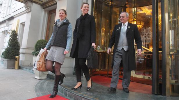 … Zwei Frauen verlassen ein Hotel, während ein Portier die Tür aufhält.