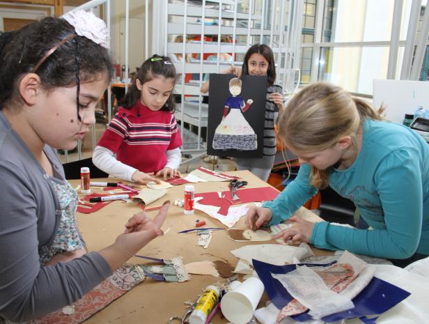 Vier Mädchen basteln an einem Tisch mit Papier, Stoffresten und Klebstoff.