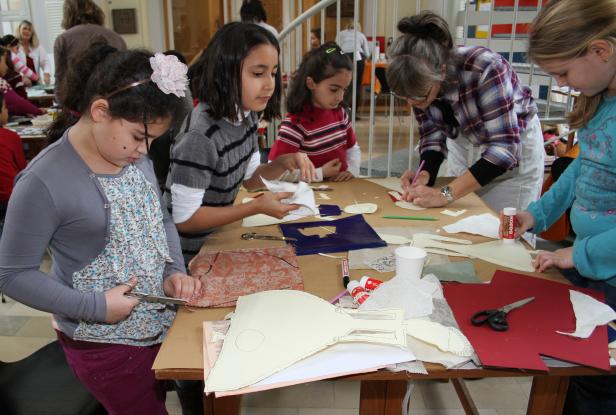 Eine Gruppe von Kindern und eine Frau basteln an einem Tisch mit Stoff und Papier.