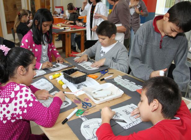 Eine Gruppe Kinder bastelt an Tischen mit Papier, Scheren und Klebstoff.
