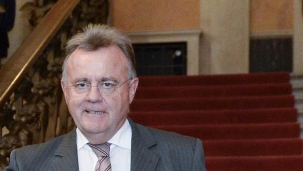 Ein Mann mit Brille und Anzug steht vor einer Treppe mit rotem Teppich.