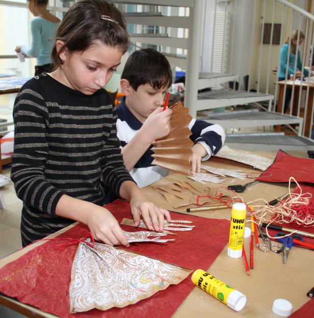 Zwei Kinder basteln an einem Tisch mit Papier, Schere und Klebstoff.
