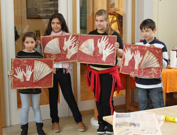 Vier Kinder präsentieren ihre Kunstwerke mit Handabdrücken und Fächern.