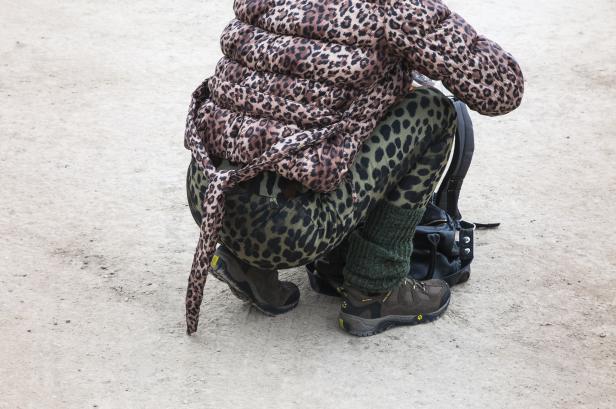 Eine Person in Leopardenmuster-Jacke und -Hose hockt neben einem schwarzen Rucksack.