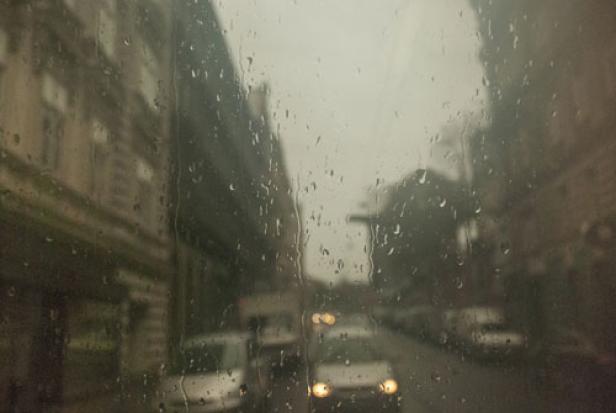 Regentropfen bedecken ein Fenster mit Blick auf eine verschwommene Stadtstraße.