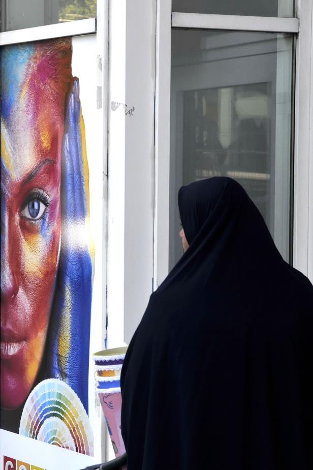 Eine Frau mit Hidschab betrachtet ein farbenfrohes Porträt und Farbmuster.