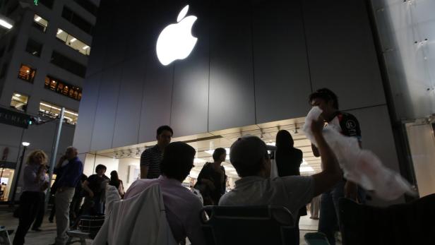 Menschen warten vor einem Apple Store bei Nacht.